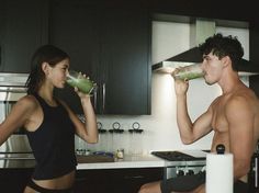 a man and woman drinking from cups in the kitchen