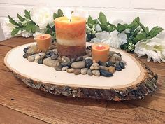 two candles sitting on top of a wooden slab with rocks and flowers in the background