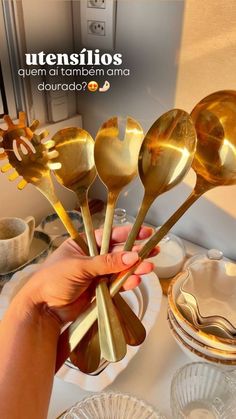 a person holding gold colored spoons in front of a table with dishes on it