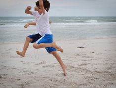 two young boys playing on the beach with their arms in the air and one jumping