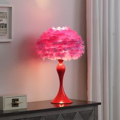 a red table lamp with pink feathers on it and a white wall in the background