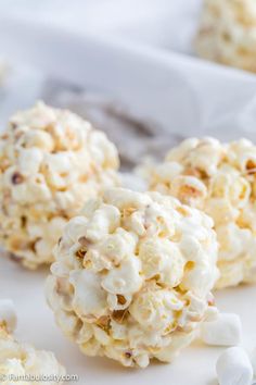 white chocolate popcorn balls with marshmallows scattered around them on a white surface