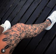 a person's legs with tattoos on them sitting on a wooden floor next to a bench