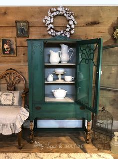 a green china cabinet with white dishes on it's shelves and an old chair