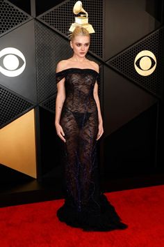 a woman standing on top of a red carpet wearing a black dress with an off the shoulder neckline