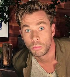 a man with blue eyes sitting in front of a plant and looking at the camera