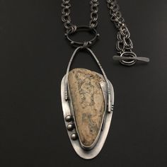 a necklace with a stone in the middle on a black surface and chain attached to it