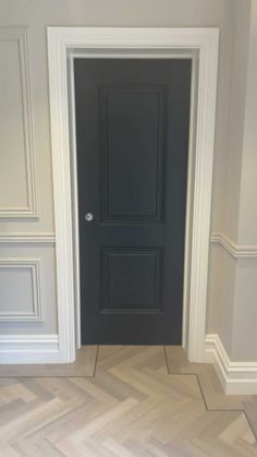 an empty room with a black door and herringbones on the floor in front of it