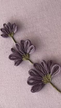 three purple flowers are sitting on top of a white cloth covered surface, with green stems sticking out of the petals