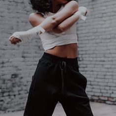 a woman in white shirt and black pants with arm wrapped around her waist standing next to brick wall