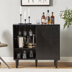 a black cabinet with liquor bottles and glasses on it in front of a wall mounted art