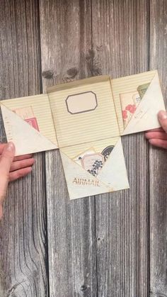 two hands holding an open envelope on top of a wooden table with wood planks