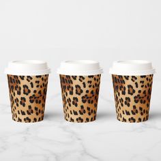 three leopard print coffee cups sitting on top of a white marble countertop next to each other