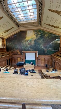 an empty room with wooden benches and a projector screen in the center, on which is a large mural