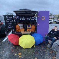 two people sitting in chairs with umbrellas and the back of an open van that has friends written on it