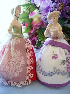 two figurines sitting next to each other on a table with flowers in the background