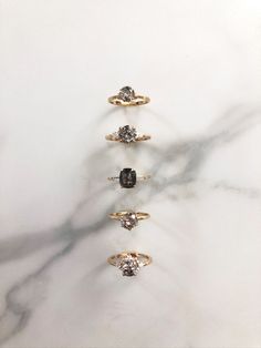 five different colored diamond rings sitting on top of a white marble surface with the shadow of a tree behind them