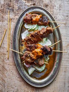 meat skewers with sauce and cucumbers on a plate