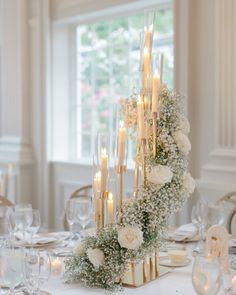 a tall centerpiece with candles and flowers on a dining room table in front of a window