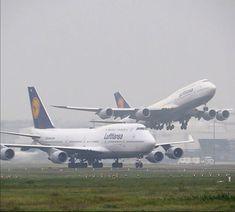 two large air planes flying in the sky above an airport runway with grass and trees