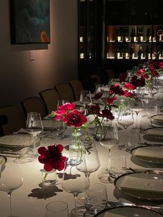 a long table is set with wine glasses, plates and red flowers in vases