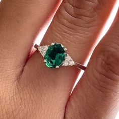 a woman's engagement ring with an oval green stone surrounded by white diamond accents