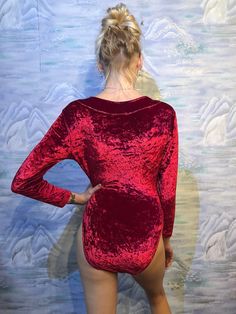 a woman wearing a red velvet bodysuit with her back to the camera and hands on her hips