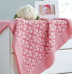 a baby's crocheted blanket on top of a dresser next to flowers