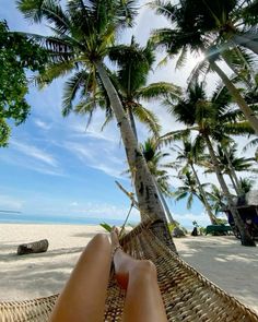 a person laying in a hammock on the beach with palm trees behind them