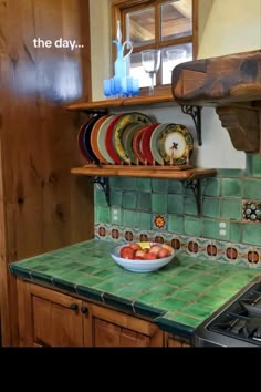 a bowl of fruit is on the counter in this kitchen with green tiles and wooden cabinets