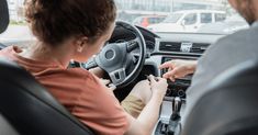 a man and woman sitting in the driver's seat of a car with their hands on the steering wheel