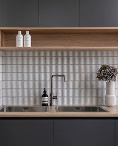 a kitchen with gray cabinets and white tile backsplashing, including a stainless steel sink