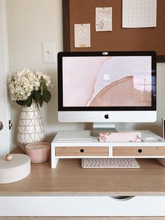 a computer monitor sitting on top of a desk next to a vase filled with flowers