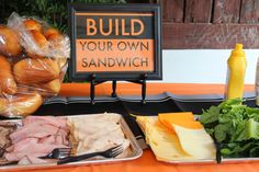 a table topped with lots of food next to a sign that says build your own sandwich