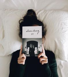 a woman laying in bed holding up a book with the cover pulled back over her face