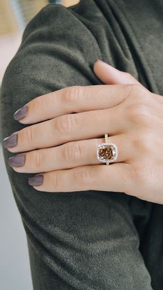 a woman's hand with a diamond ring on her left and brown nail polish