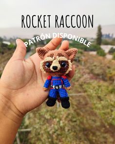 a hand holding a small crocheted raccoon toy in it's left hand