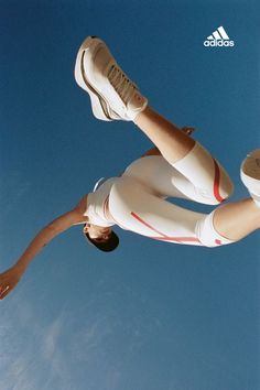 a woman in white pants and sneakers doing a trick on a skateboard with her feet up