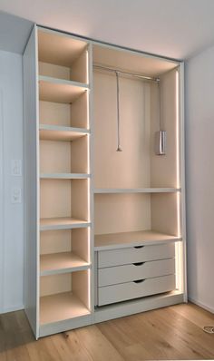 an empty white closet with drawers and lights on the shelves, in front of a door