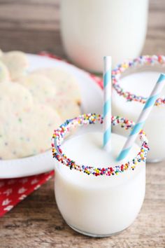 two glasses filled with milk and sprinkles next to cookies on a plate