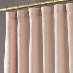 pink curtains hanging on a gold rod in front of a gray wall and white walls