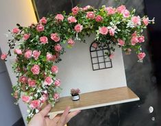 a person holding up a fake house with pink roses on the outside and green plants growing out of it