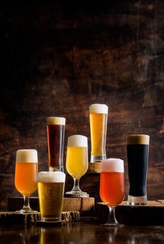 several different types of beer are lined up on a wooden table in front of a dark wood wall