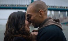 a man and woman standing next to each other in front of a bridge