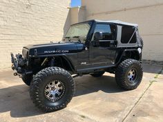 a black jeep is parked in front of a brick building with large tires and rims