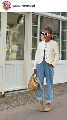 a woman standing in front of a store holding a purse and wearing sunglasses on her head