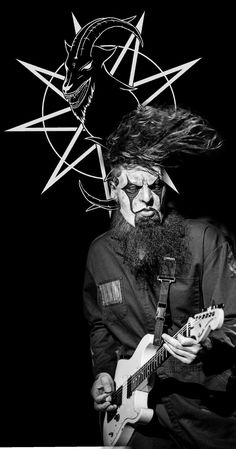 a black and white photo of a man with long hair playing an electric guitar in front of a demon