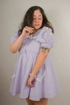 You and this dress go together like peanut butter and jelly! Turn heads in our delectable gingham Grape Gumdrop Dress. Our new vibrant take on our Gumdrop Dress for Spring has white daisies on the puff sleeves. This classic dress has a lace trimmed collar and heart shaped pockets. Other fresh flavors to add to your basket are also available. Model wearing size L. Sweet Gingham Dress For Spring, Fitted Lace Trim Dress For Picnic, Cute Vintage Spring Dress For Daywear, Cute Vintage Dress For Spring Daywear, Short Sleeve Prairie Dress With Lace Trim For Spring, Puff Sleeve Dress With Ruffle Hem For Picnic, Spring Prairie Dress With Lace Trim And Short Sleeves, Gumdrop Dress, Sweet Gingham Dress With Ruffles