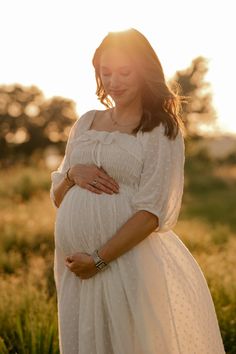 a pregnant woman wearing a white dress in the sun, with her hands on her belly