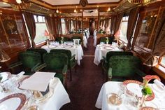 a dining car on a train with green velvet chairs and white tablecloths set for dinner